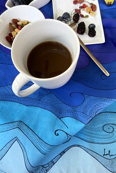 Ocean waves tea towel with a cup of coffee and a plate of raspberry and nuts