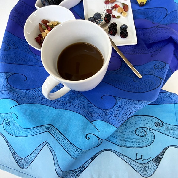 Ocean waves tea towel with a cup of coffee and a plate of raspberry and nuts