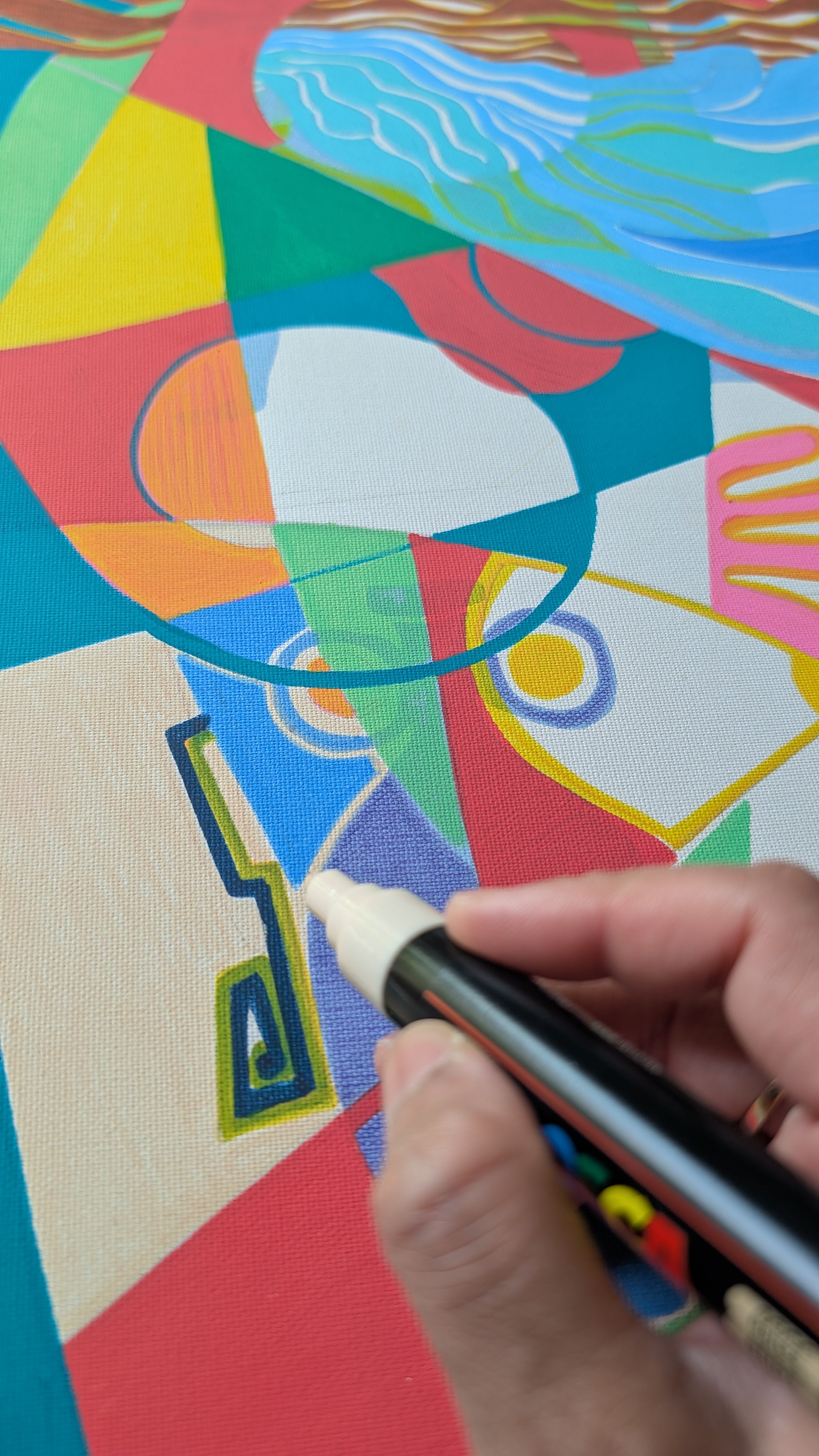A close-up of a hand holding a black marker with a white tip, drawing on a colorful abstract canvas painting.
