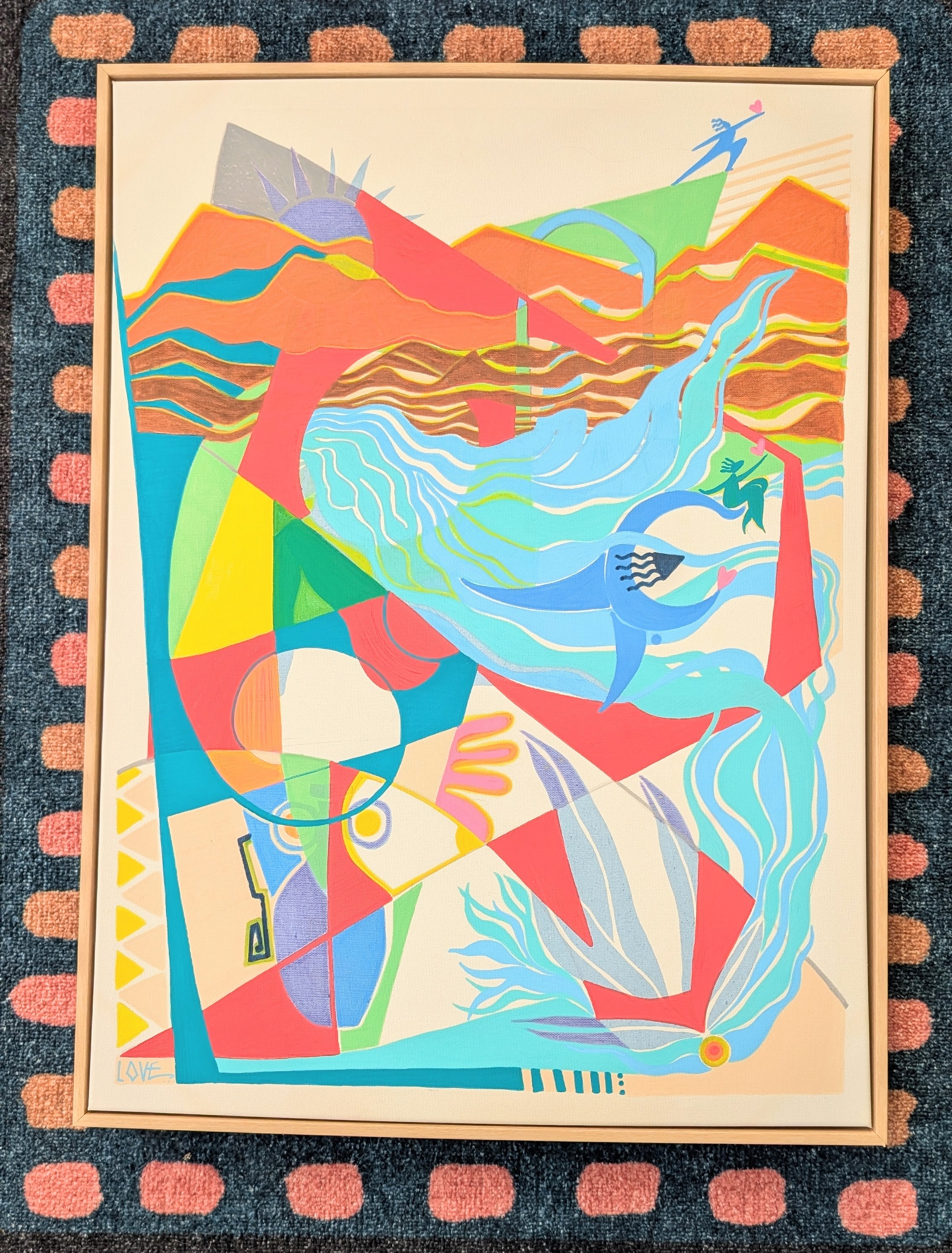 A framed abstract art print featuring a vibrant, geometric composition with flowing blue and red shapes, set against a dark patterned rug. By Loveleen Saxena 