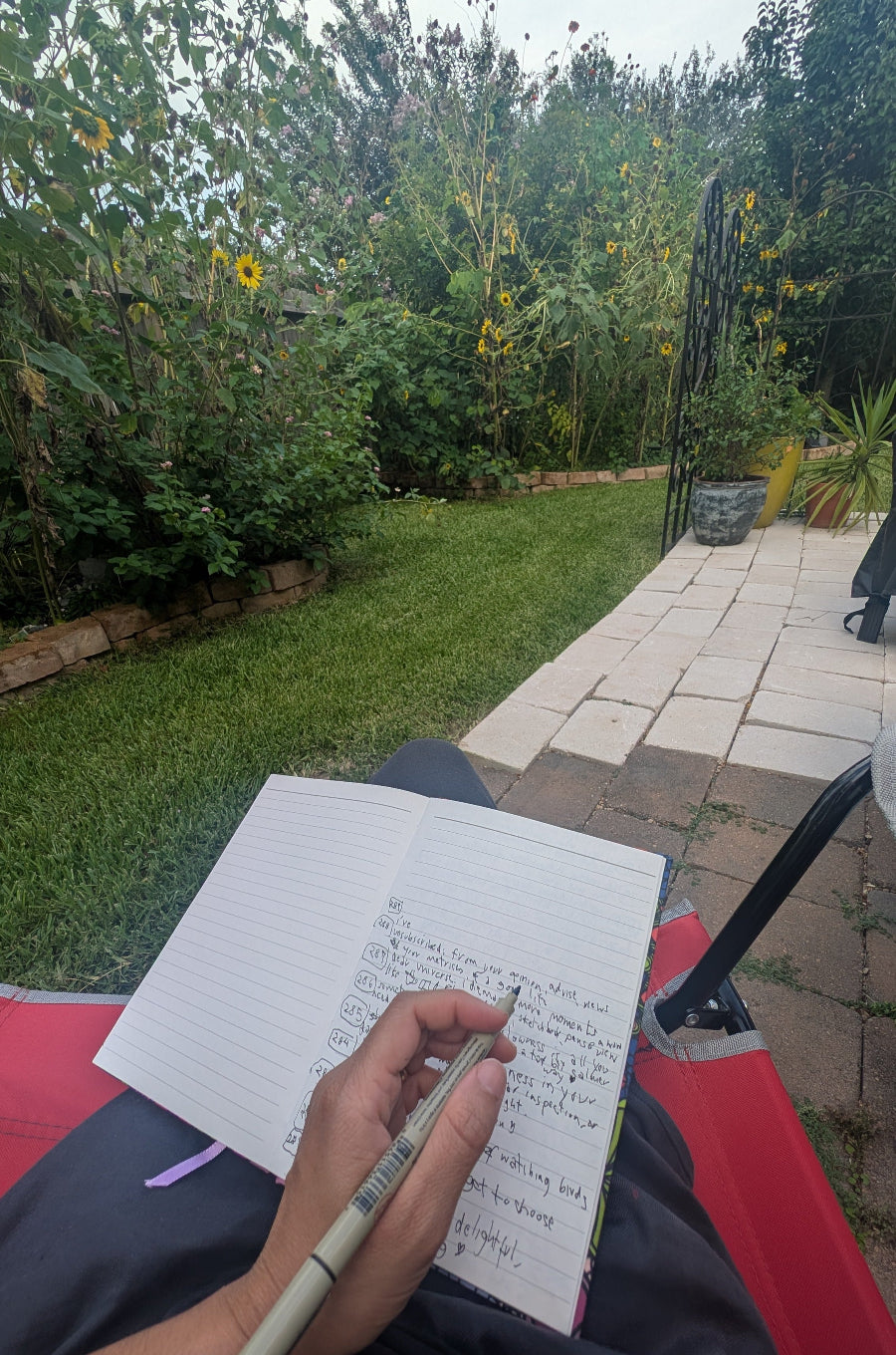 Person writing in a notebook outdoors with greenery in the background