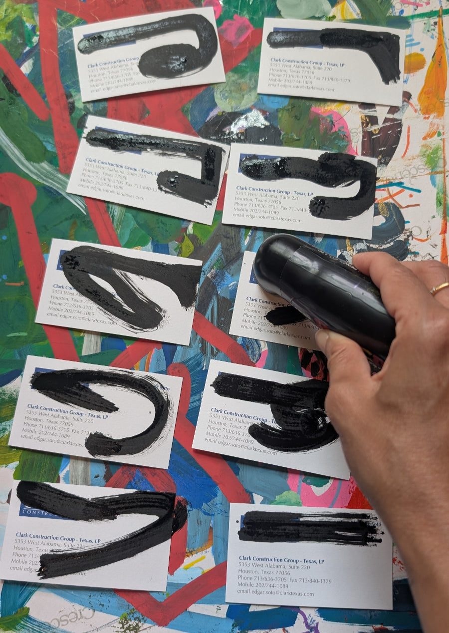 Hand holding a black object over printed images of similar objects on a colorful surface
